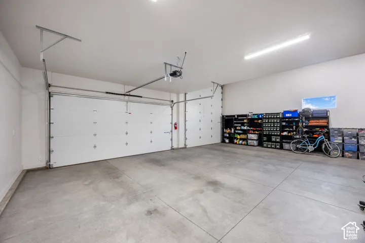 Expansive three-car garage featuring a smooth concrete floor, white paneled overhead door, high-output linear lighting, and a horizontal transom window