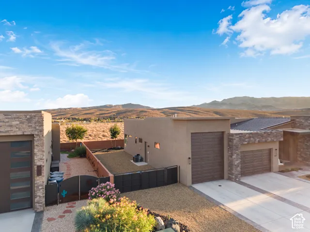 Modern exterior featuring stone veneer accents, stucco siding, multi-panel garage doors, and xeriscaped grounds with mountain backdrop
