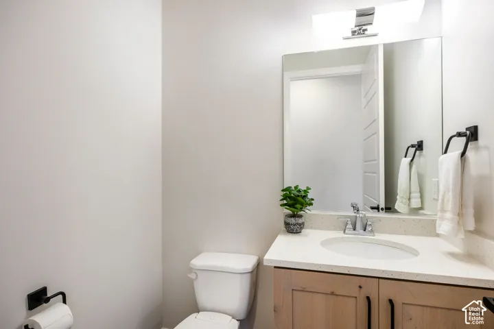 Vanity with light-toned wood cabinetry, stone-composite countertop, oval undermount sink, and matte black hardware