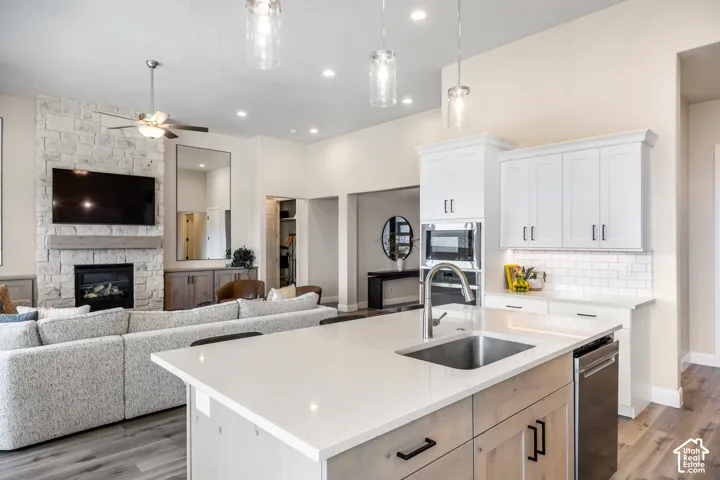 Kitchen featuring a quartz-topped island with an integrated stainless steel sink, white cabinetry with subway tile backsplash, and built-in wall oven