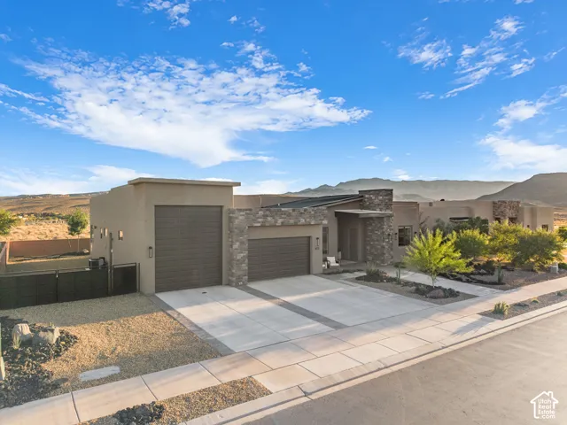 Contemporary residence featuring a stucco exterior, natural stone veneer accents, multi-car garage, low-maintenance desert landscaping, and prominent mountain backdrop