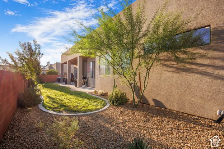 Stucco exterior, covered patio, manicured lawn with concrete curbing, gravel landscaping, and decorative desert plantings