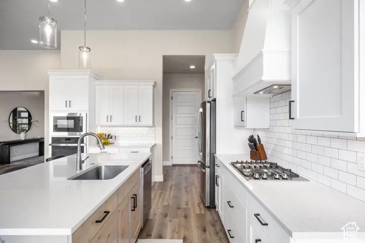 Kitchen featuring white shaker cabinetry, quartz countertops, a subway tile backsplash, stainless steel gas cooktop with a custom range hood, and wood-finish flooring