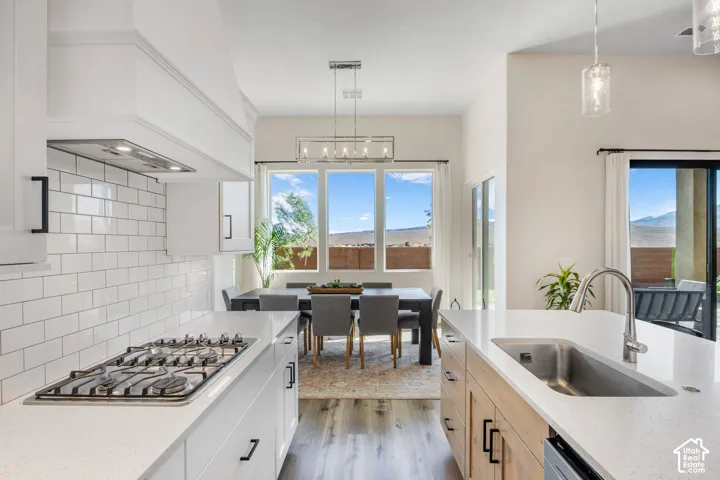 Kitchen featuring a central island with a solid-surface countertop and undermount stainless steel sink, white subway tile backsplash, gas cooktop with a custom range hood, and wood-finish flooring
