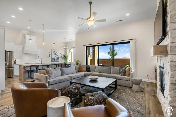 Open-concept living space featuring wood-finish flooring, a floor-to-ceiling stone-surround fireplace with a timber mantel, recessed lighting, and large sliding glass doors