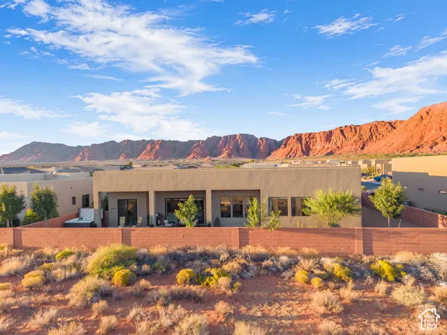 Stucco exterior residence featuring a covered patio, red masonry perimeter wall, and built-in hot tub, set against a red rock mountain backdrop