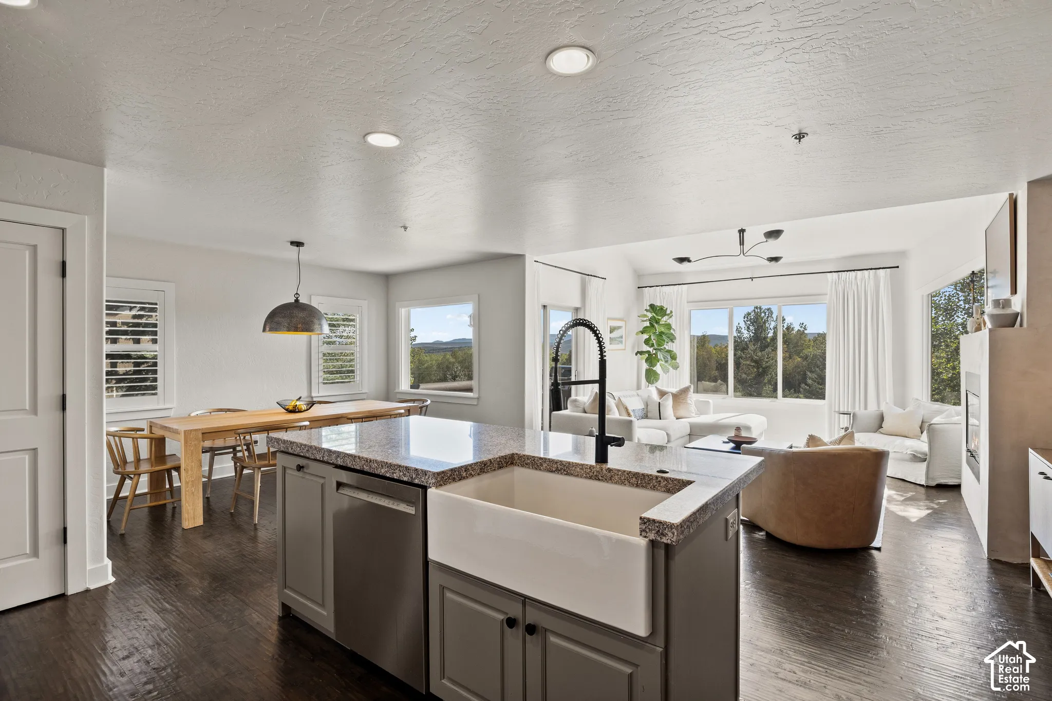 Kitchen island with a farmhouse sink and granite countertop, wood-finish flooring, recessed lighting, and a dining area with a pendant light fixture