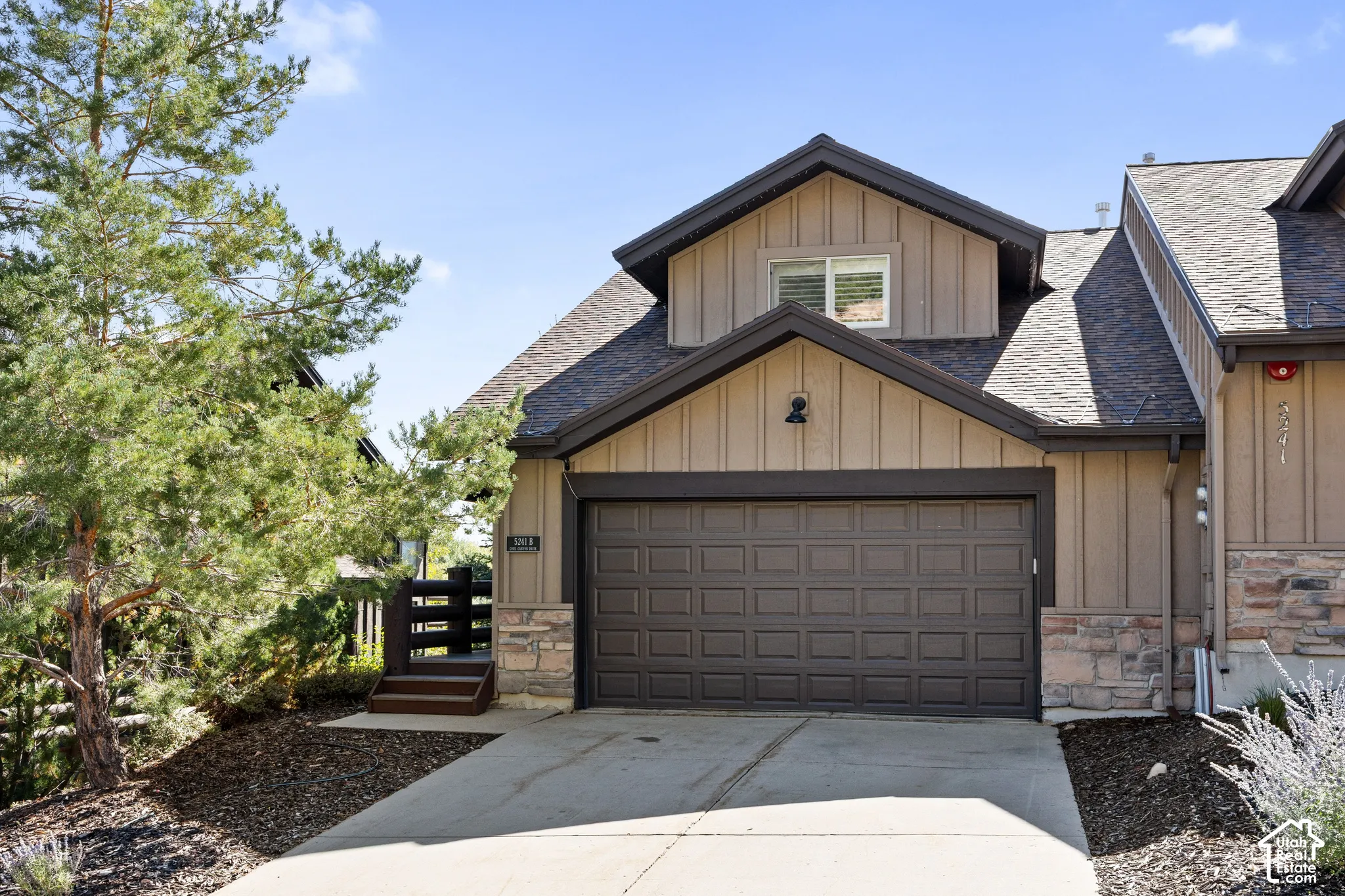 Attached two-car garage with a panel door, stone accents on the facade, and a dormer window