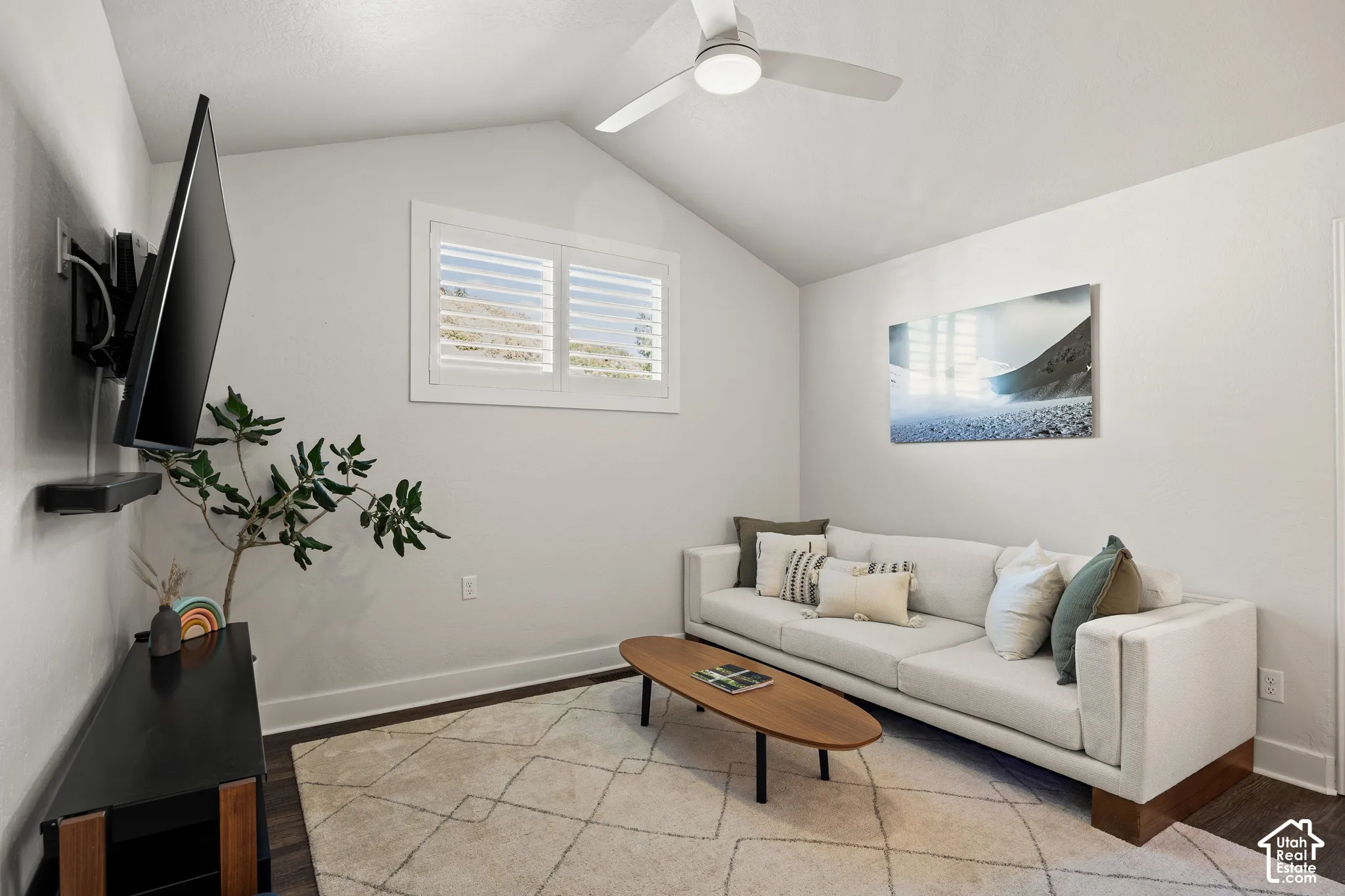 Vaulted ceiling with a ceiling fan, window with plantation shutters, dark wood-finish flooring, and a wall-mounted television bracket