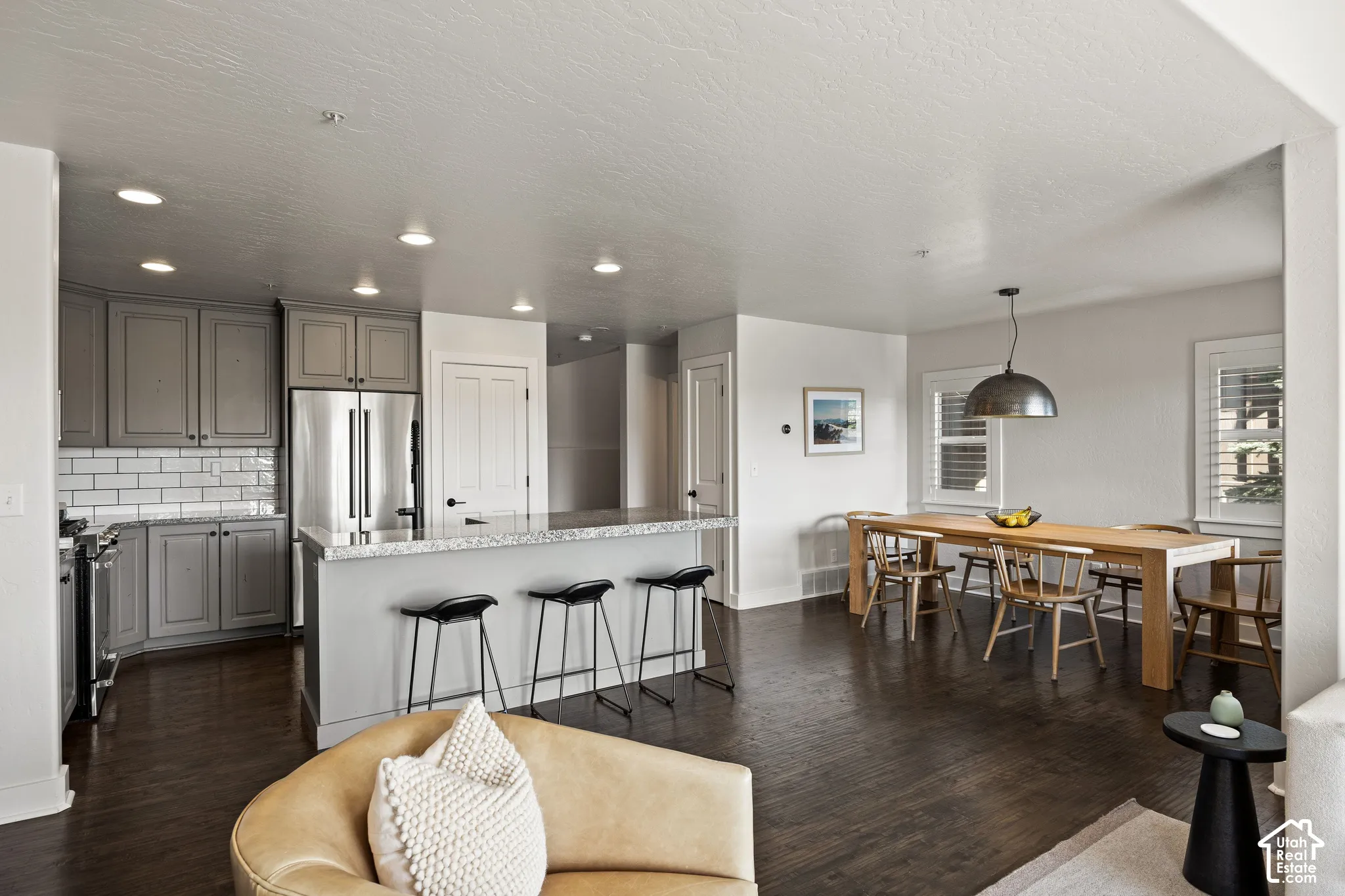 Open-concept living space with dark wood-finish flooring, recessed lighting, and a kitchen island featuring a granite-style countertop