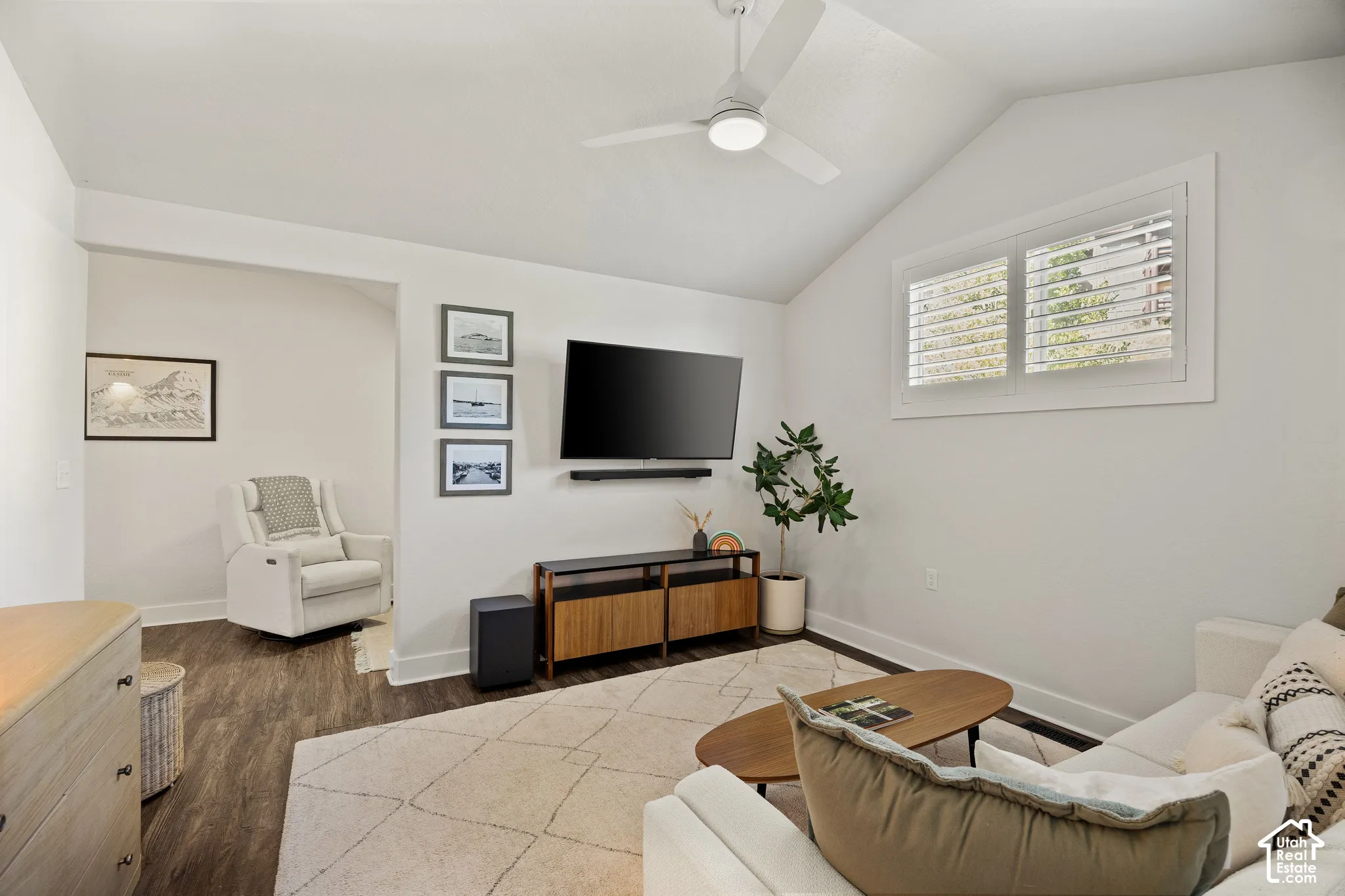 Vaulted ceiling, wood-finish flooring, ceiling fan, built-in window shutters, and a wood-finish media console
