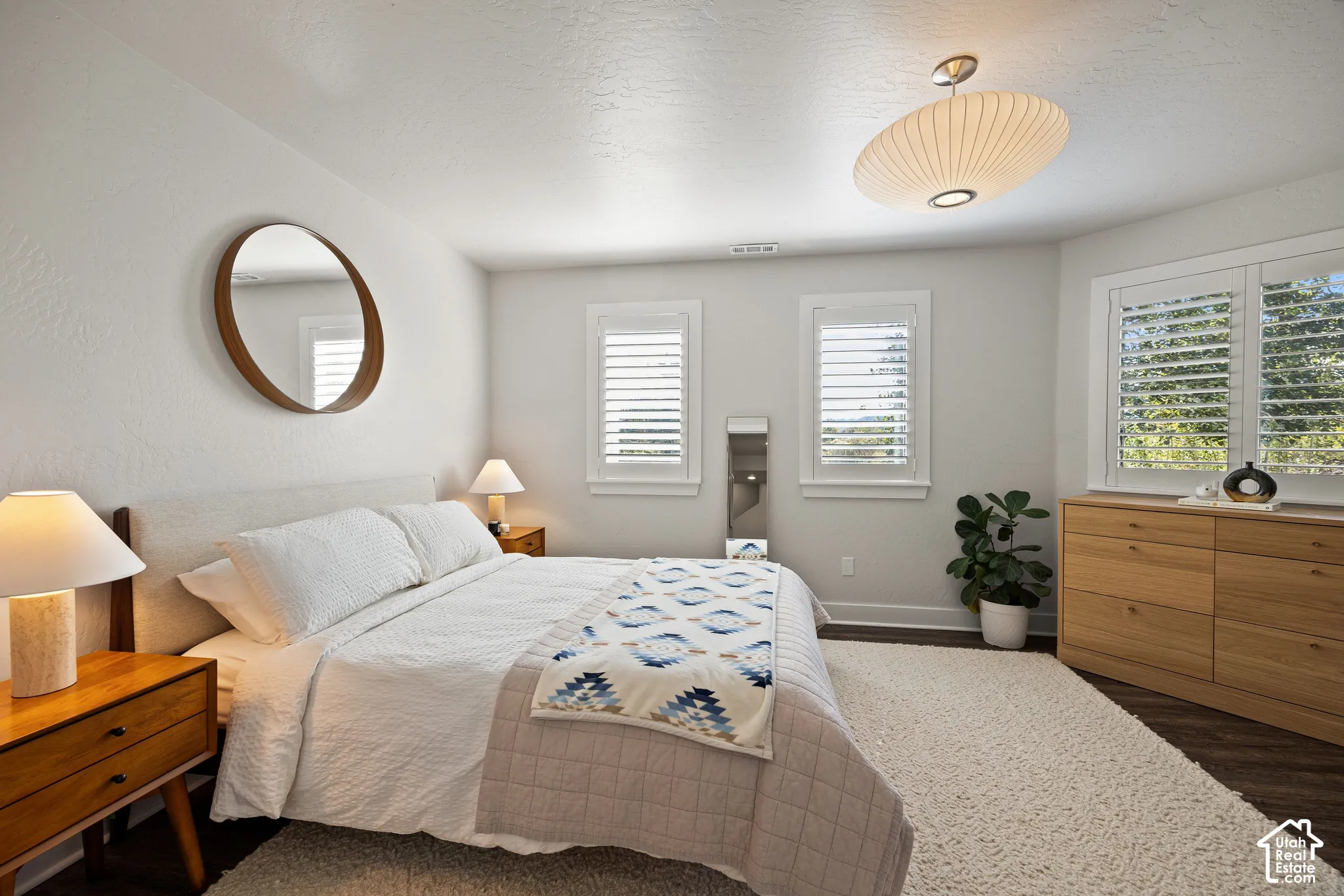 Bright room featuring multiple windows with louvered shutters, wood-finish flooring, and a unique overhead light fixture