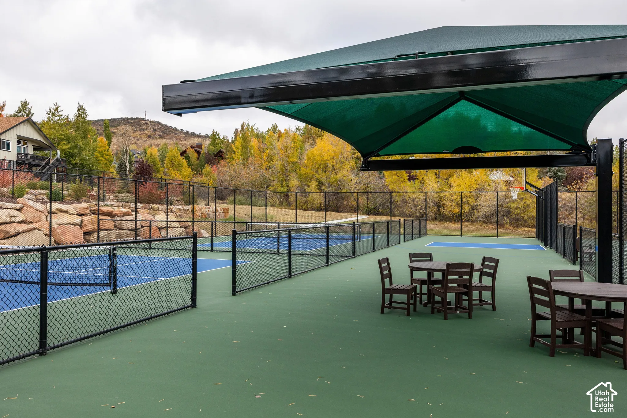 Outdoor recreational court with multiple playing areas, shaded seating, and perimeter fencing