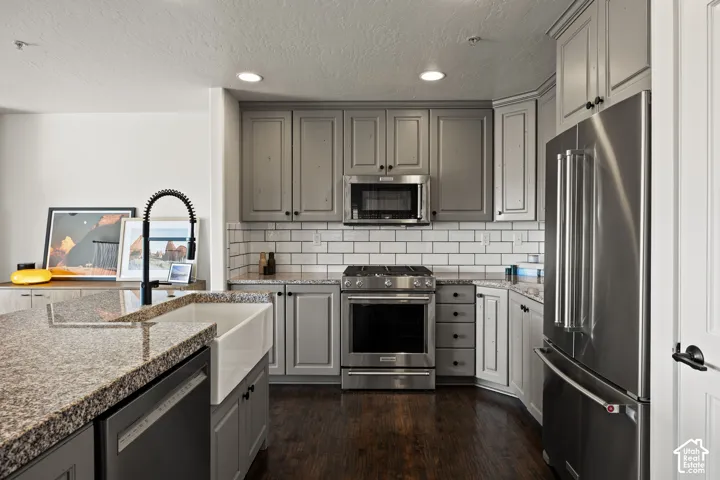 Kitchen featuring granite countertops, a farmhouse sink, stainless steel appliances, dark wood-finish flooring, and subway tile backsplash