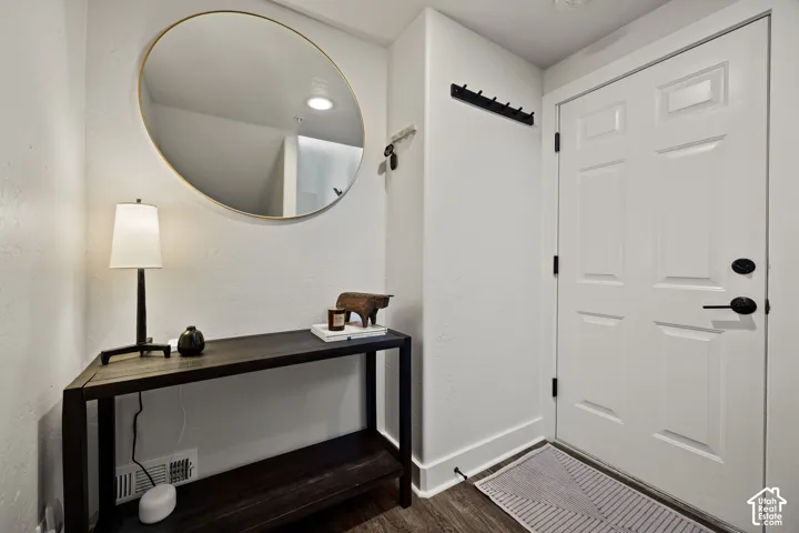 Paneled entry door with matte black hardware, wood-finish flooring, and a built-in coat rack