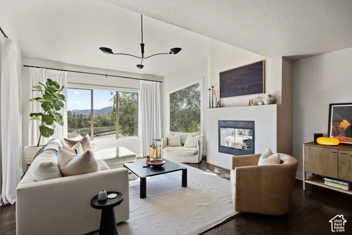 Wood-finish flooring, a contemporary fireplace with a dark-framed insert, and large windows with surrounding scenery