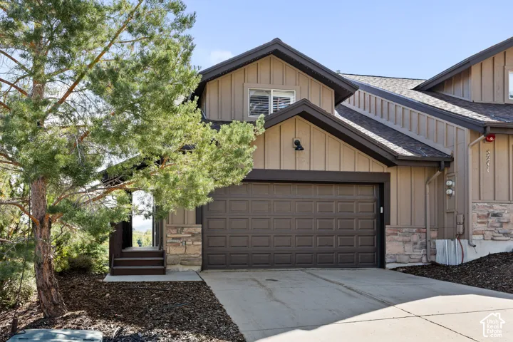 Exterior featuring board and batten siding, stone accents, a multi-pane garage door, and a paved driveway