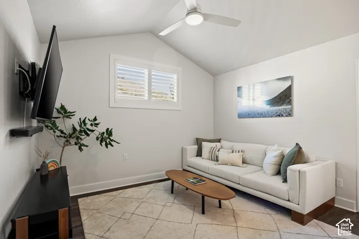 Vaulted ceiling with a ceiling fan, window with plantation shutters, dark wood-finish flooring, and a wall-mounted television bracket