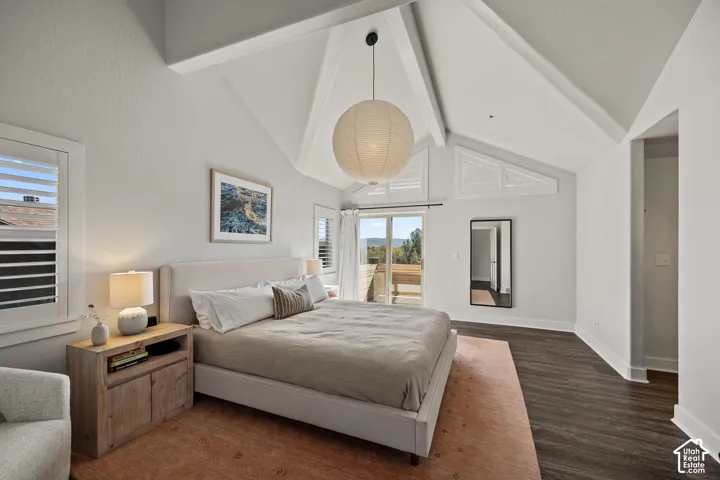 Vaulted ceiling with exposed beams, dark wood-finish flooring, white plantation shutters, and sliding glass door to exterior