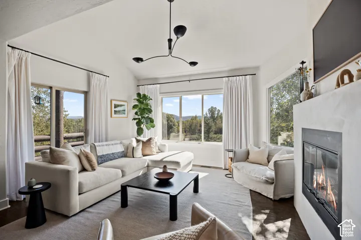 Vaulted ceiling, modern chandelier, integrated fireplace, expansive windows, wood-finish flooring