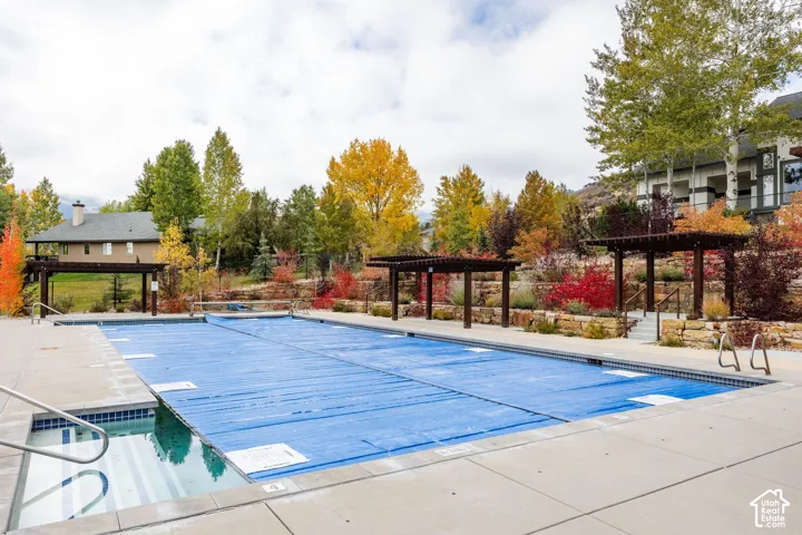 Outdoor swimming pool featuring a tiled spa with stainless steel handrails, expansive pool decking, and two pergolas
