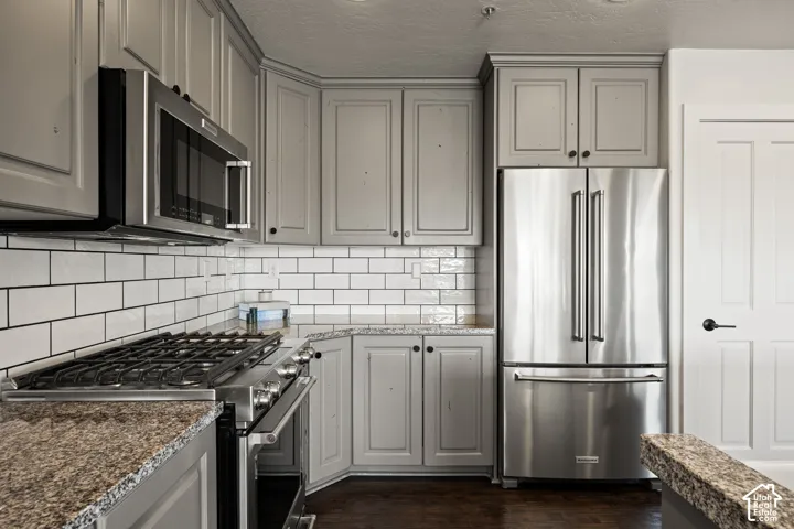 Gray cabinetry, stainless steel appliances, subway tile backsplash, and wood-finish flooring
