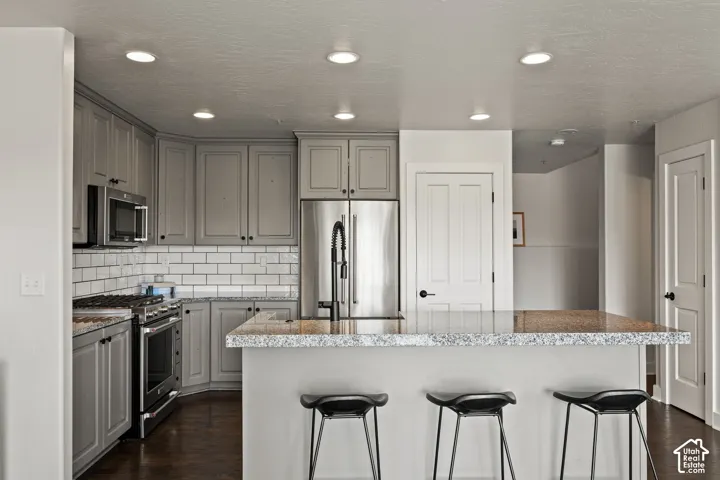 Kitchen featuring gray cabinetry, stainless steel appliances, white subway tile backsplash, recessed lighting, and a peninsula with a stone-finish countertop