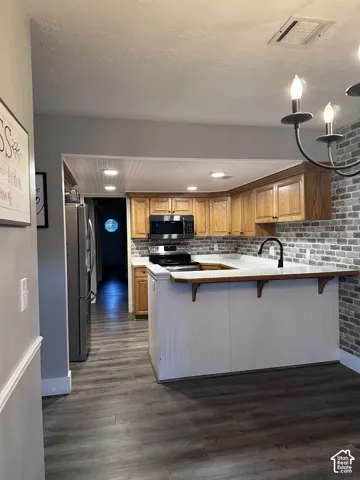 Kitchen featuring wood cabinetry, brick-patterned backsplash, white peninsula with beadboard detailing, wood-finish flooring, and a built-in microwave