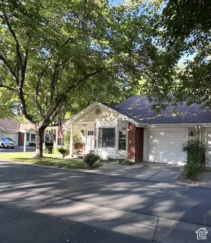 Exterior featuring a gabled roofline, partial brick masonry, concrete driveway, attached garage, and mature tree canopy
