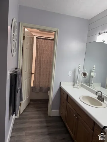 Bathroom featuring wood-finish flooring, a wood vanity with a white countertop, an integrated sink with a metallic faucet, a large wall-mounted mirror, and horizontal shiplap wall paneling
