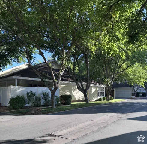 Exterior featuring horizontal siding, dark shingled roof, white vinyl privacy fencing, mature trees, and detached garage