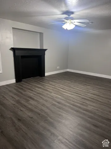 Wood-finish flooring, fireplace with a black surround and mantel, built-in recessed wall niche, and a multi-light ceiling fan