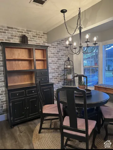 Textured brick accent wall paired with wood-finish flooring, bay window with integrated blinds, and multi-arm chandelier