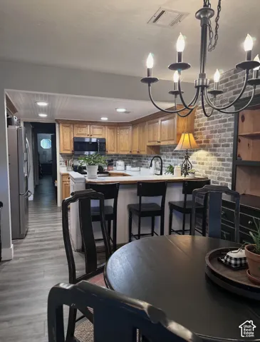 Kitchen featuring natural wood cabinetry, a decorative brick backsplash, recessed lighting, and a peninsula with breakfast bar seating
