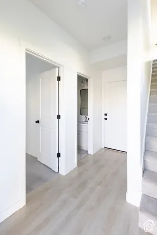 Interior hall featuring wood-finish flooring, white panel doors with matte black hardware, recessed lighting, and carpeted stairs