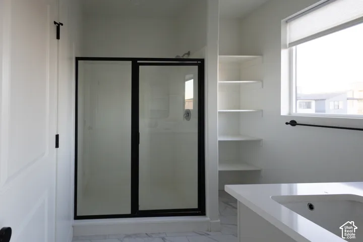 Walk-in shower with black-frame glass enclosure, built-in shelving, white quartz vanity countertop, and stone-pattern tile flooring