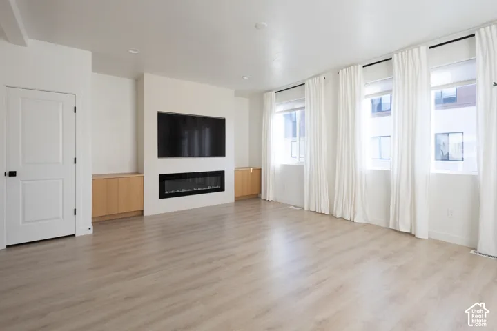 Living area featuring wood-finish flooring, a linear electric fireplace, built-in cabinetry, and large windows with recessed lighting
