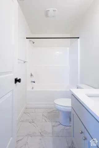 Bathroom featuring a vanity with a white countertop, tub and shower combination with chrome fixtures, and large-format stone-patterned tile flooring