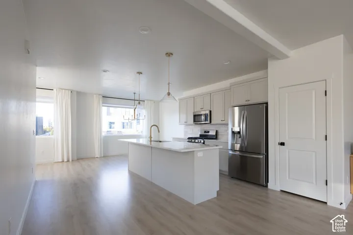 Kitchen featuring a quartz-topped island, light-toned cabinetry, stainless steel appliances, pendant lighting, and wood-finish flooring