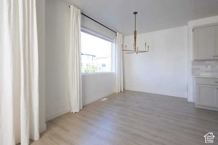 Open-concept space featuring wood-finish flooring, a large window, a modern tiered metal chandelier, and gray shaker-style cabinetry with neutral tile backsplash