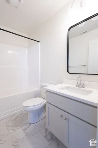 Bathroom featuring a vanity with light-toned cabinetry, solid surface countertop, rectangular undermount sink, and a rectangular mirror with a black frame, complemented by tile flooring and a white tub-shower combination