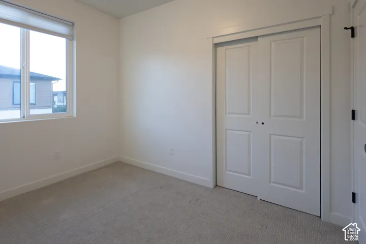 Neutral-toned carpeted flooring, large window, and double-panel sliding closet doors with crisp white trim