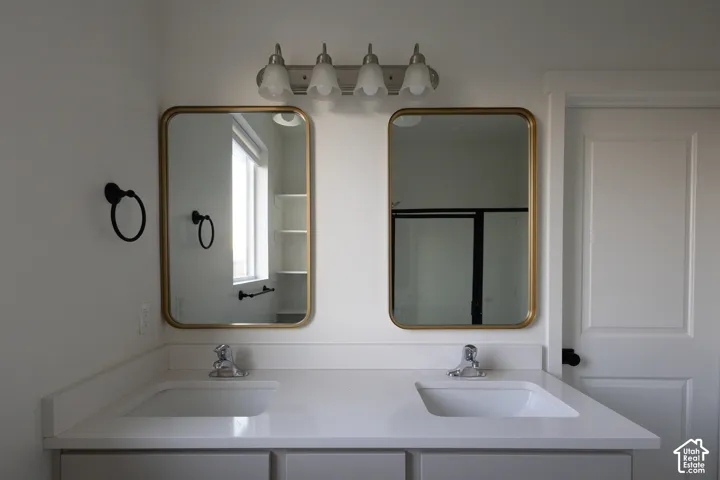 Dual-sink vanity featuring a white surface, rectangular undermount basins, gold-toned rectangular wall mirrors, and four-light overhead vanity fixture