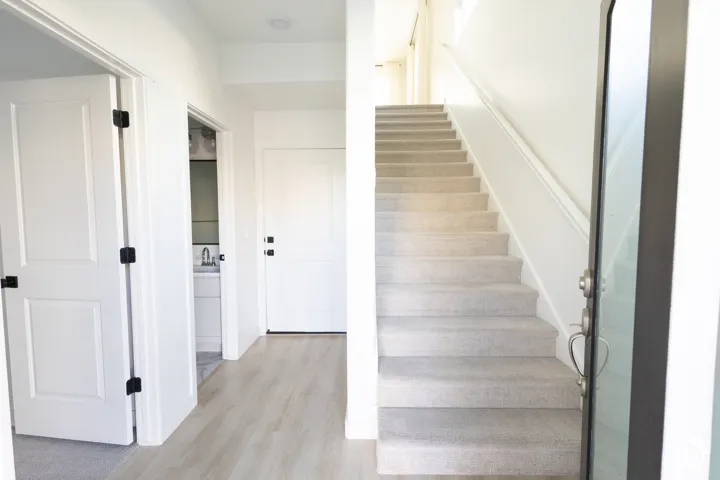 Entryway featuring wood-finish flooring, a carpeted staircase with a white railing, panel doors with matte black hardware, and recessed ceiling lighting
