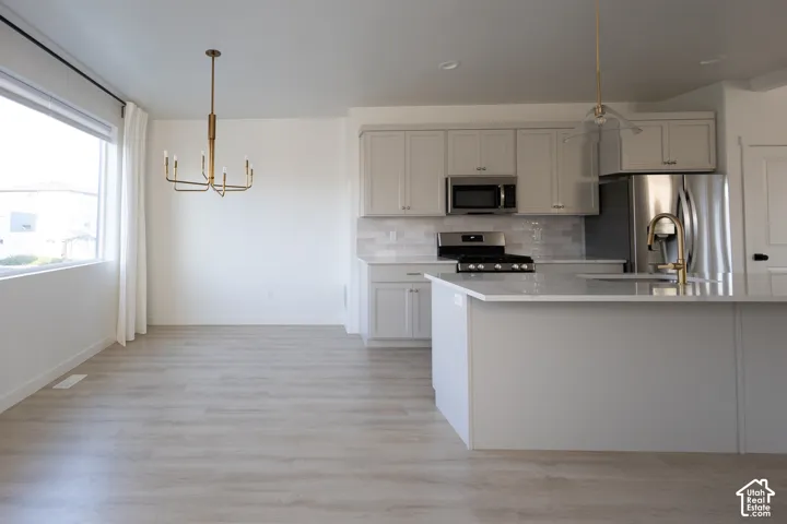 Kitchen featuring light-toned cabinetry, quartz countertops, subway tile backsplash, stainless steel appliances, and wood-finish flooring