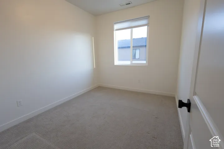 Room featuring neutral-toned carpeting, off-white wall finishes, a single-pane sliding window with a minimalist blind, and a door equipped with matte black hardware