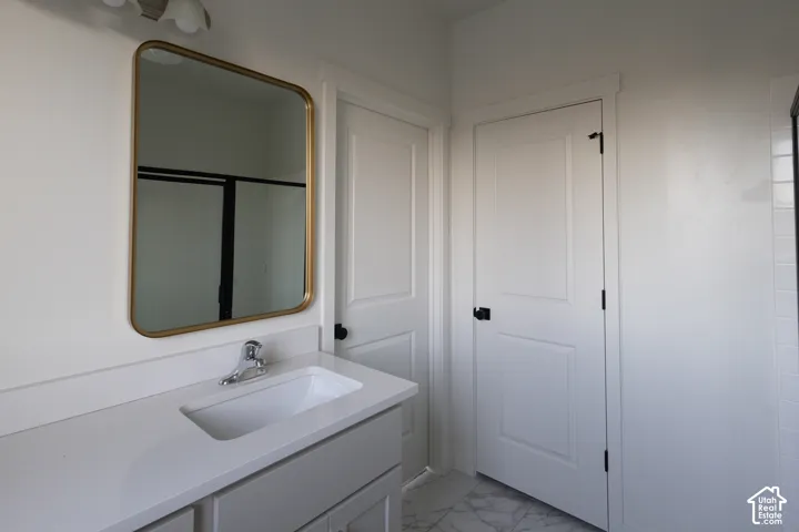 Bathroom vanity featuring a quartz countertop with an integrated rectangular sink, gold-toned rounded-edge mirror, two-panel interior doors with matte black hardware, and stone-pattern tile flooring