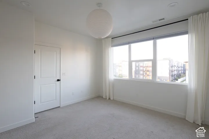 Neutral-toned carpeted flooring, large window, spherical pendant light fixture, and interior panel door