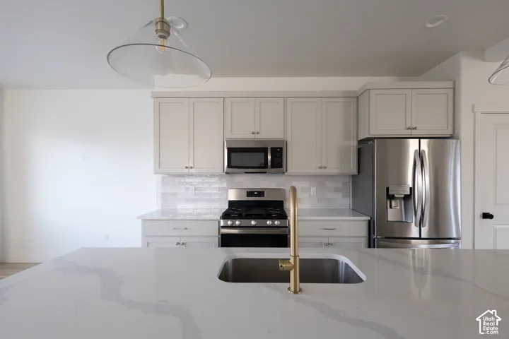 Kitchen featuring a central island with a solid surface countertop, undermount sink, and brass-finish faucet, complemented by light-toned shaker cabinetry, stainless steel appliances, and a subway tile backsplash