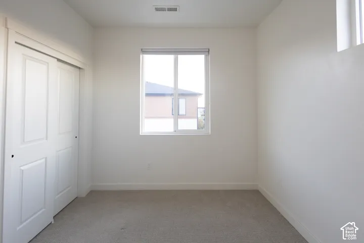 Neutral-toned carpeting, sliding closet doors, and a single-pane window with a roller shade